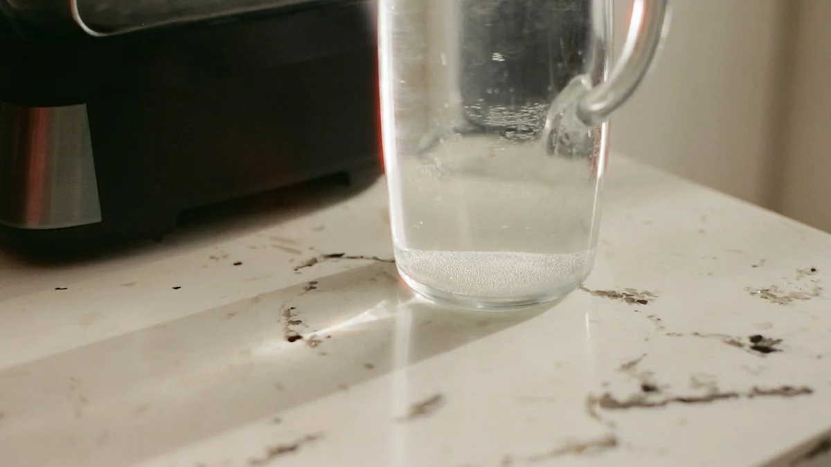 A clear glass pitcher of water on a marble kitchen counter beside a stainless steel countertop appliance