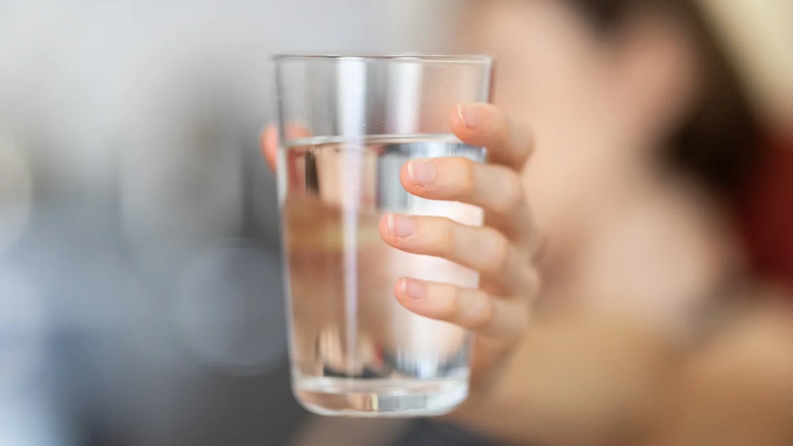 A person holding up a clear glass of filtered drinking water