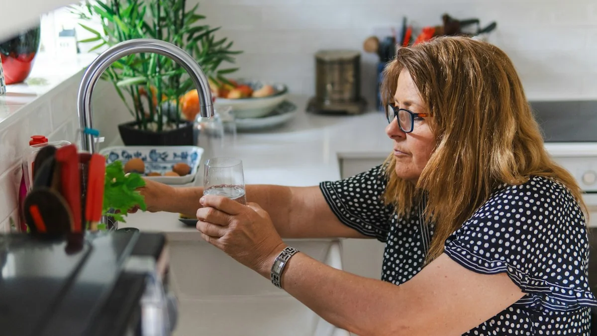 A woman filling a drinking glass at a kitchen faucet, the first-draw sample step of testing home tap water