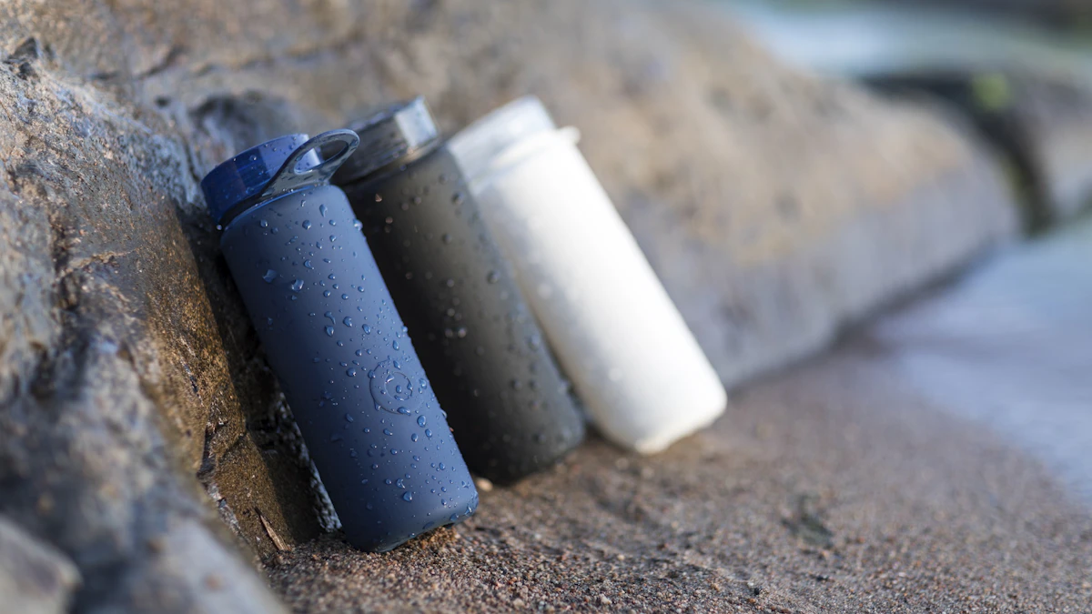 A row of water filter cartridges of different types arranged next to a glass of clear water