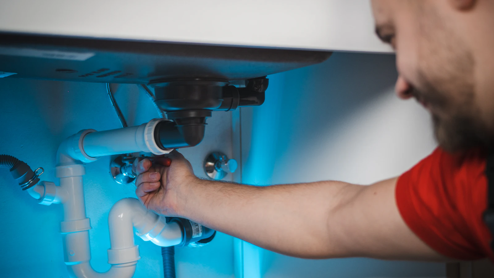 Person working on plumbing connections under a kitchen sink