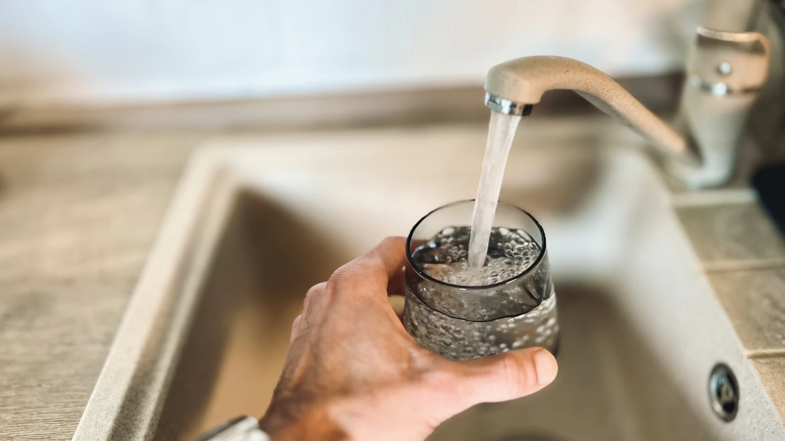 Hand filling a glass of water from a kitchen faucet